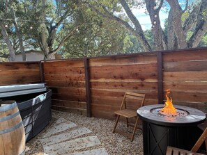 Eine Holzterrasse mit Grill, einem runden Tisch und einem Feuerkorb sowie einem Stuhl.