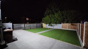 Un patio trasero con un piso empedrado, un césped y una valla de madera.