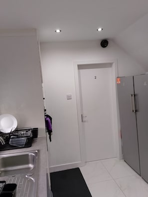 A modern kitchen with a stainless steel sink, a dish rack, and a refrigerator. - The Salford House (Salford)
