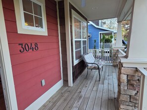 En træterrasse med en stenvæg, et husnummer '3048', og en stol med pude.