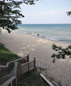 A beach with a wooden walkway leading to the shore, a lifebuoy on the railing, and a clear view of the ocean.