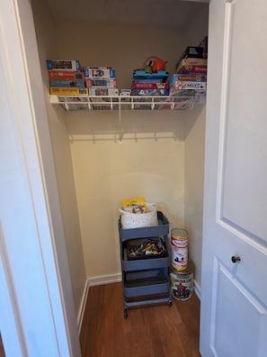 A storage area with shelves holding various board games and puzzles, a small cart with toys and a can of paint.