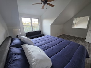 A bedroom with a bed, a window, a ceiling fan, and a door.
