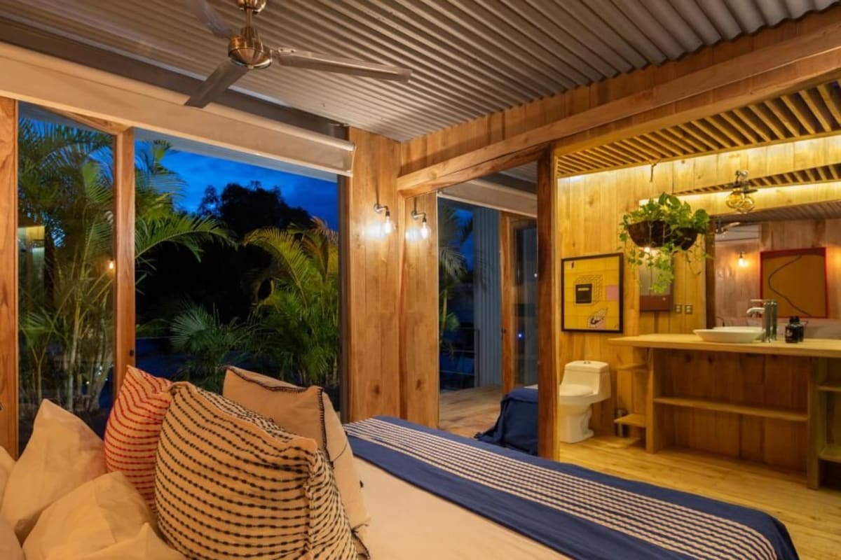 A bedroom with a bed, pillows, a ceiling fan, and a view of the outdoors.