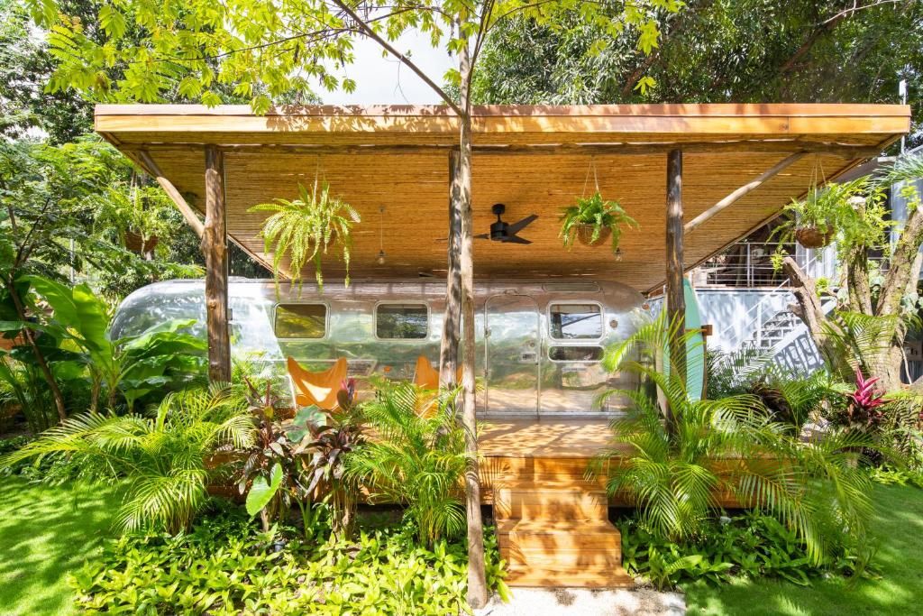 A covered outdoor area with a wooden structure, surrounded by lush greenery and a parked vehicle.
