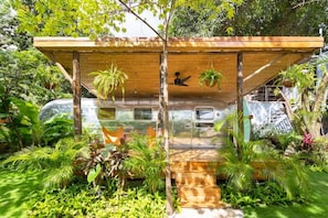 A covered outdoor area with a wooden structure, surrounded by lush greenery and a parked vehicle. - House of Somos, Santa Teresa (Santa Teresa)