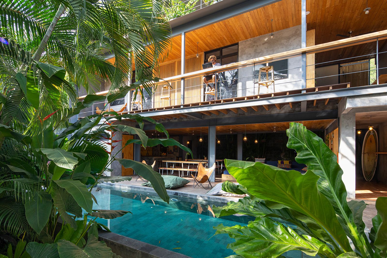 A modern multi-level building with a pool surrounded by tropical plants.