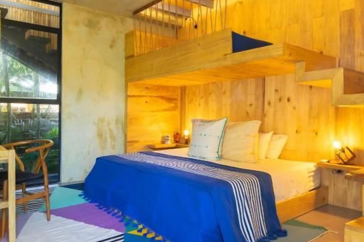 A bedroom with a bunk bed, a bedside table, a lamp, and a view of the outdoors.