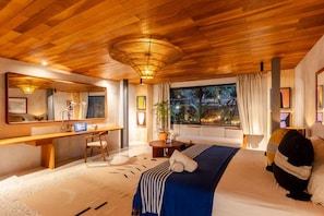 A hotel room with a wooden ceiling, a bed with a blue bedspread, a desk with a computer, a chair, and a window with curtains. - House of Somos, Santa Teresa (Santa Teresa)