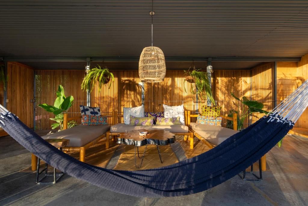 Un hamac dans une pièce meublée de meubles en bois, avec un luminaire suspendu en fibres tressées et des plantes.