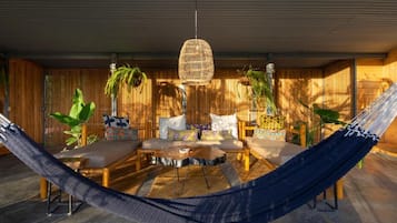 Un hamac dans une pièce meublée de meubles en bois, avec un luminaire suspendu en fibres tressées et des plantes.