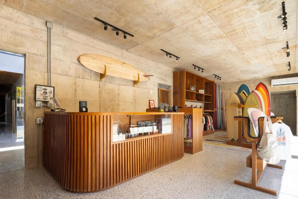 A reception area with a wooden counter, a surfboard, and a clothing rack with various items.
