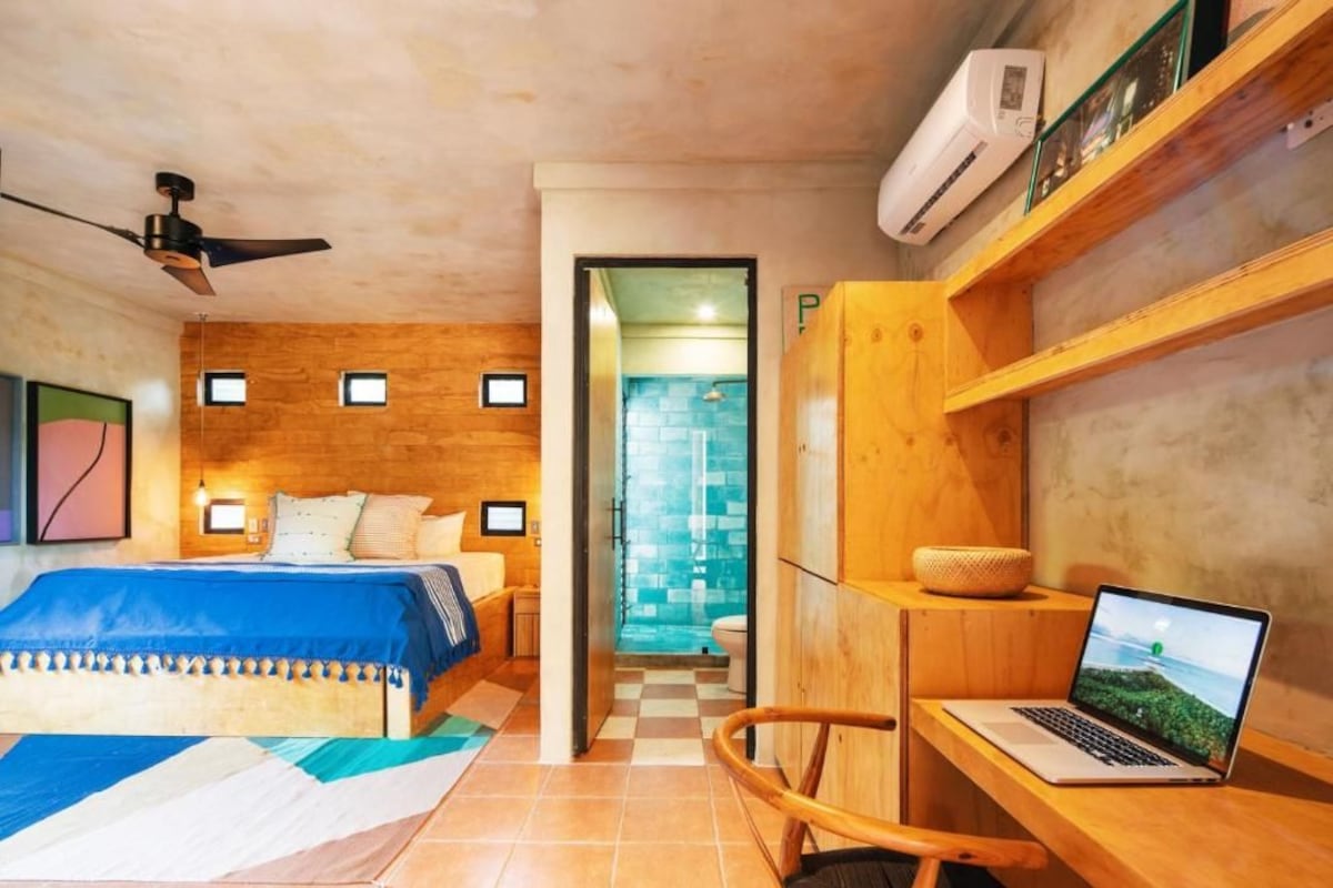 A bedroom with a bed, a desk with a laptop, a ceiling fan, and an air conditioning unit.
