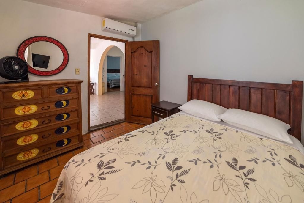 Un dormitorio con cama de madera, cómoda con cajones decorativos, espejo y unidad de aire acondicionado.