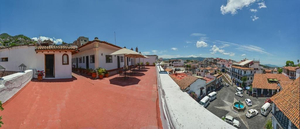 Une terrasse sur le toit avec un sol rouge, un petit bâtiment doté d  ’une porte, et une vue sur une ville avec ses bâtiments et un ciel dégagé.
