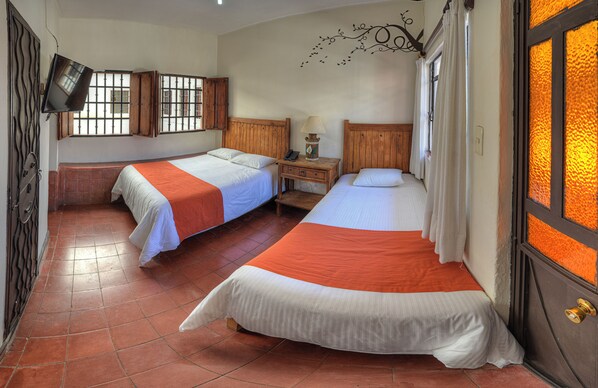 A hotel room with two beds, a wooden nightstand, a small table, and a television mounted on the wall.