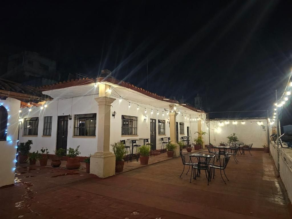 Un patio al aire libre con mesas y sillas, plantas en macetas y luces colgantes.