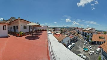 Una terraza en la azotea con suelo rojo, un edificio pequeño con tejado de tejas y vistas a un pueblo con edificios y cielo despejado.