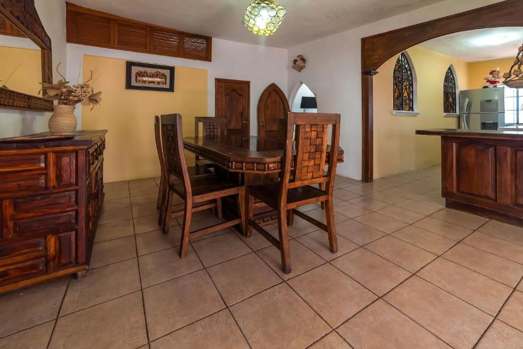 Un comedor con una mesa y sillas de madera, una encimera de cocina y un jarrón decorativo sobre un mueble.