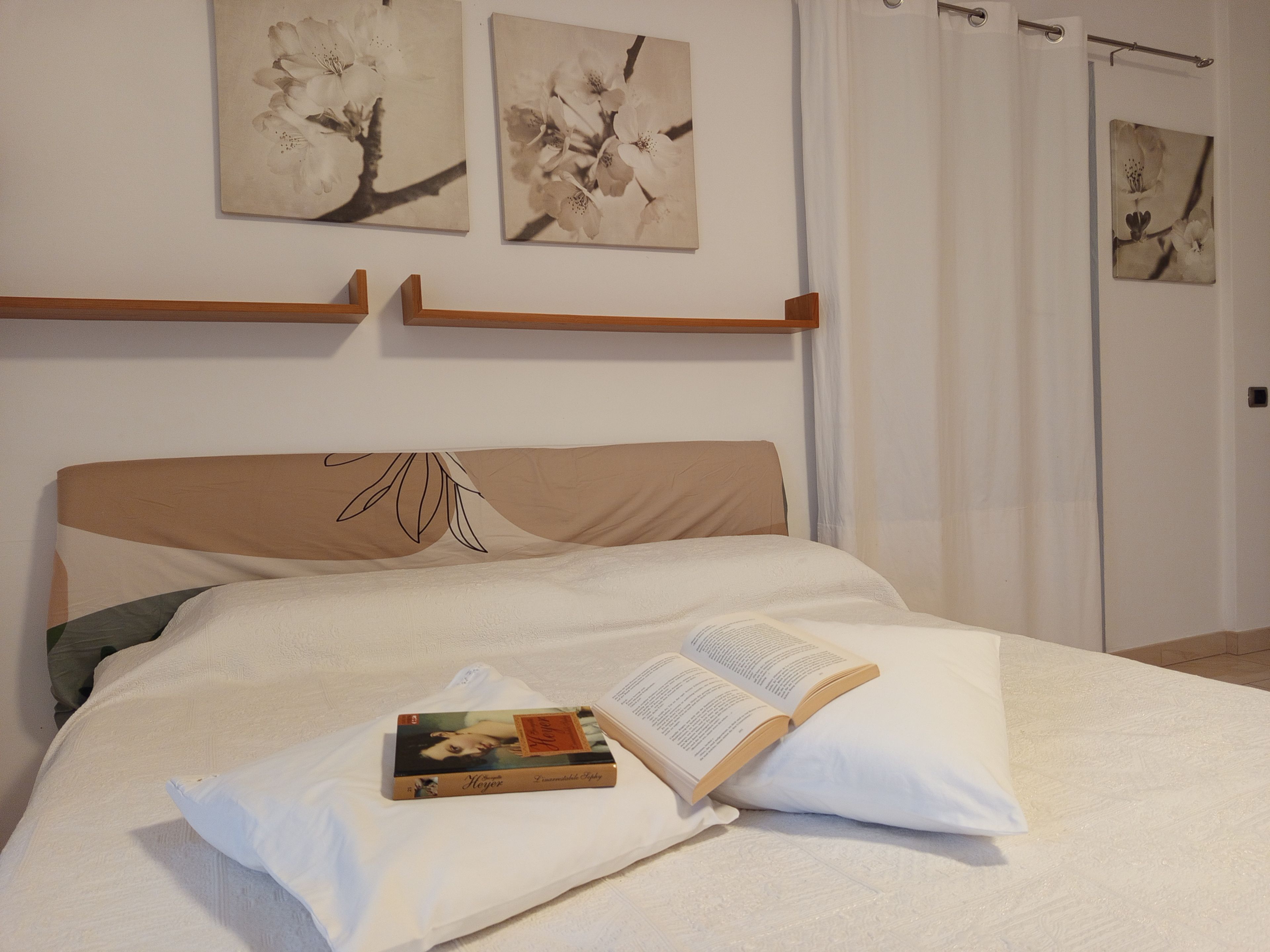 Een opgemaakt bed met een boek en een kussen, een houten hoofdbord en kunstwerken aan de muur.