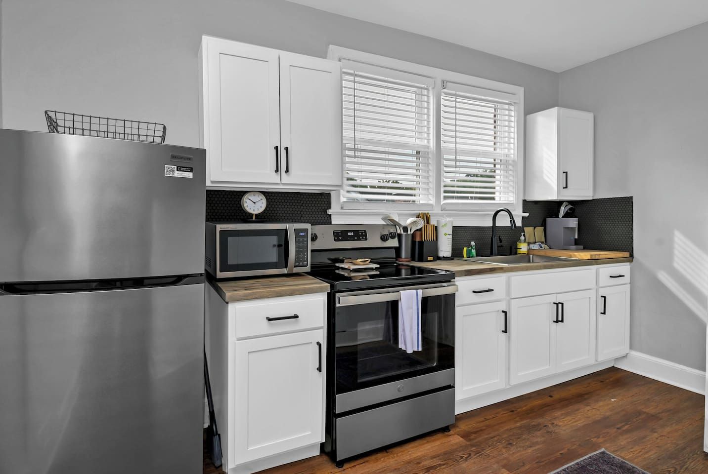 A modern kitchen with white cabinets, stainless steel appliances, and a wooden countertop.
