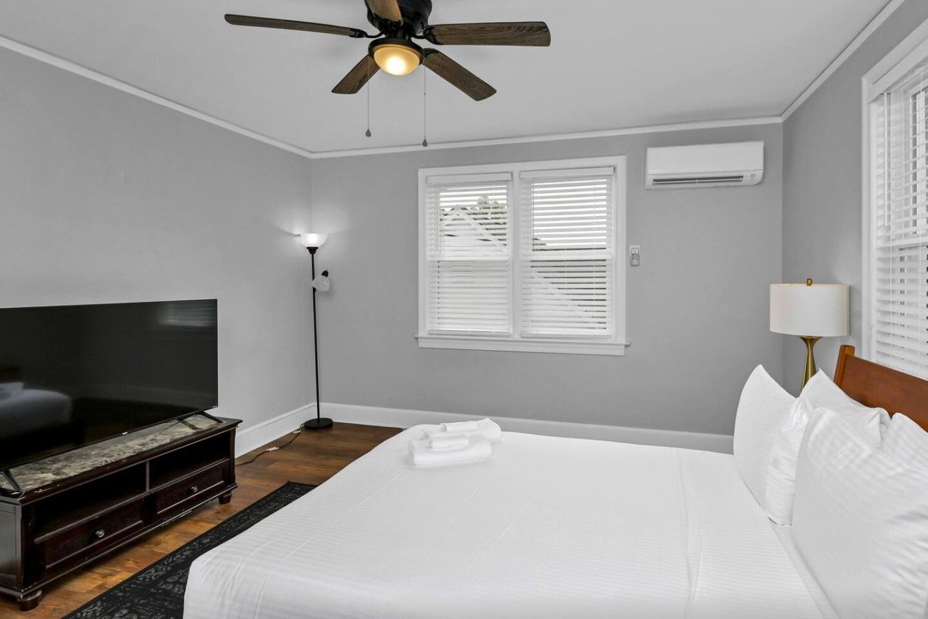 A hotel room with a bed, a television, a ceiling fan, and a window with blinds.