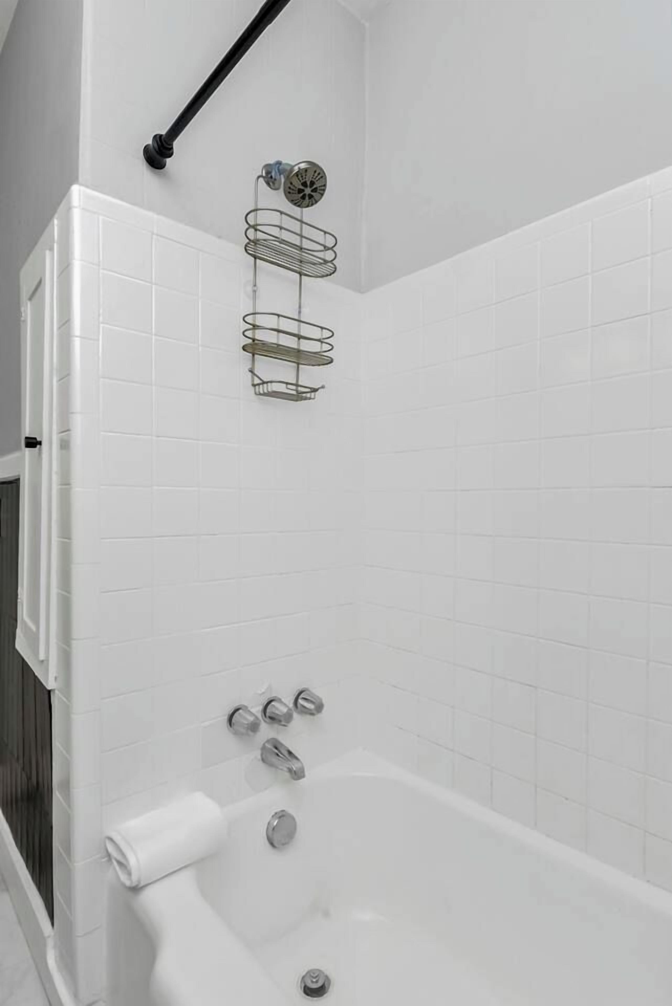 A bathroom with white tiled walls, a bathtub, and a metal towel rack.
