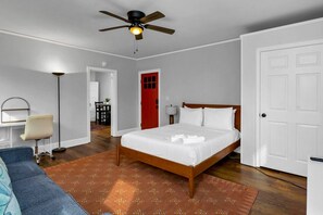 Ett hotellrum med en säng, ett skrivbord, en stol, en takfläkt och en röd dörr.