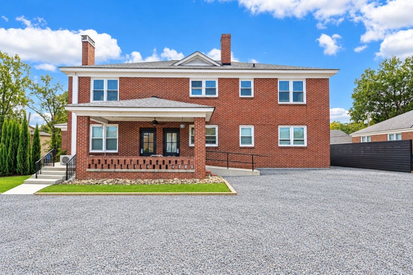A two-story brick house with a front porch, a driveway, and a fenced yard.