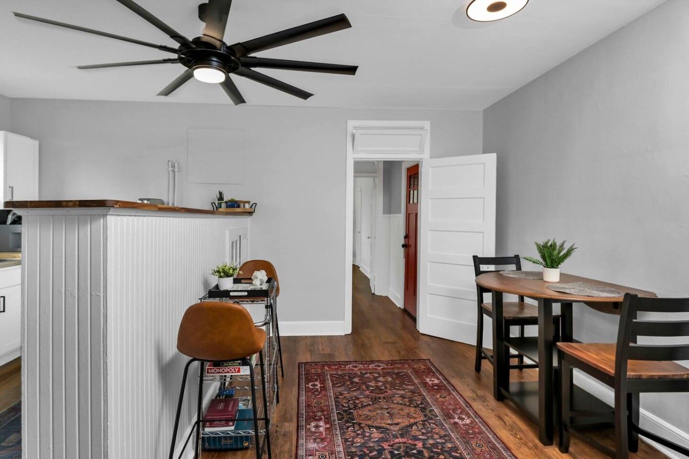 A dining area with a table, chairs, a ceiling fan, and a red patterned rug.
