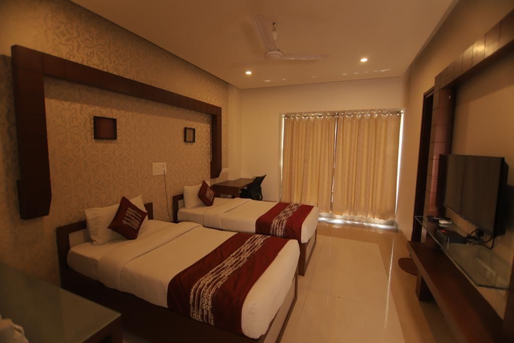 Habitación de hotel con dos camas, televisión y ventana con cortinas.