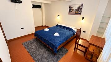Une chambre d’hôtel comprenant un lit, un bureau, une chaise, un tapis, un tableau accroché au mur et un appareil fixé au plafond.