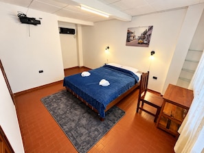 Une chambre d’hôtel comprenant un lit, un bureau, une chaise, un tapis, un tableau accroché au mur et un appareil fixé au plafond.