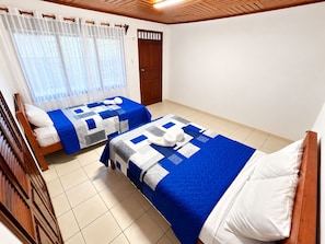 Une chambre d’hôtel avec deux lits, une tête de lit en bois, une fenêtre avec des rideaux légers et une porte avec un cadre en bois.