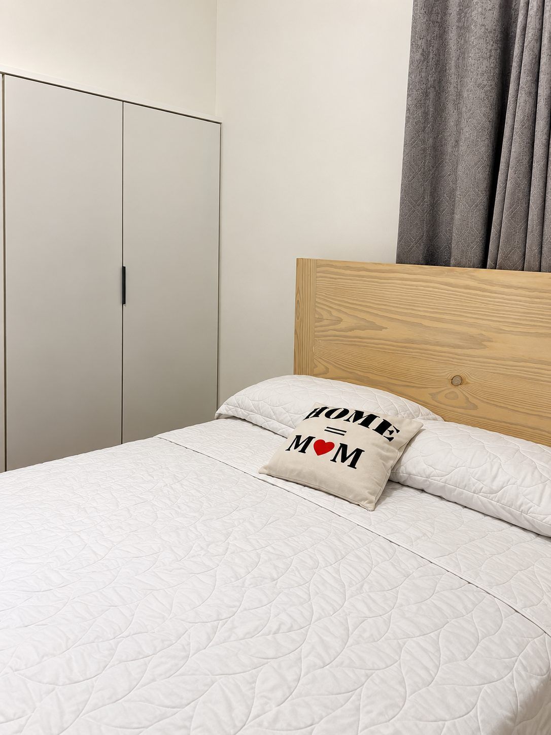 Een slaapkamer met een bed, een kussen met de tekst 'HOME = MOM', een houten hoofdbord en een kledingkast.