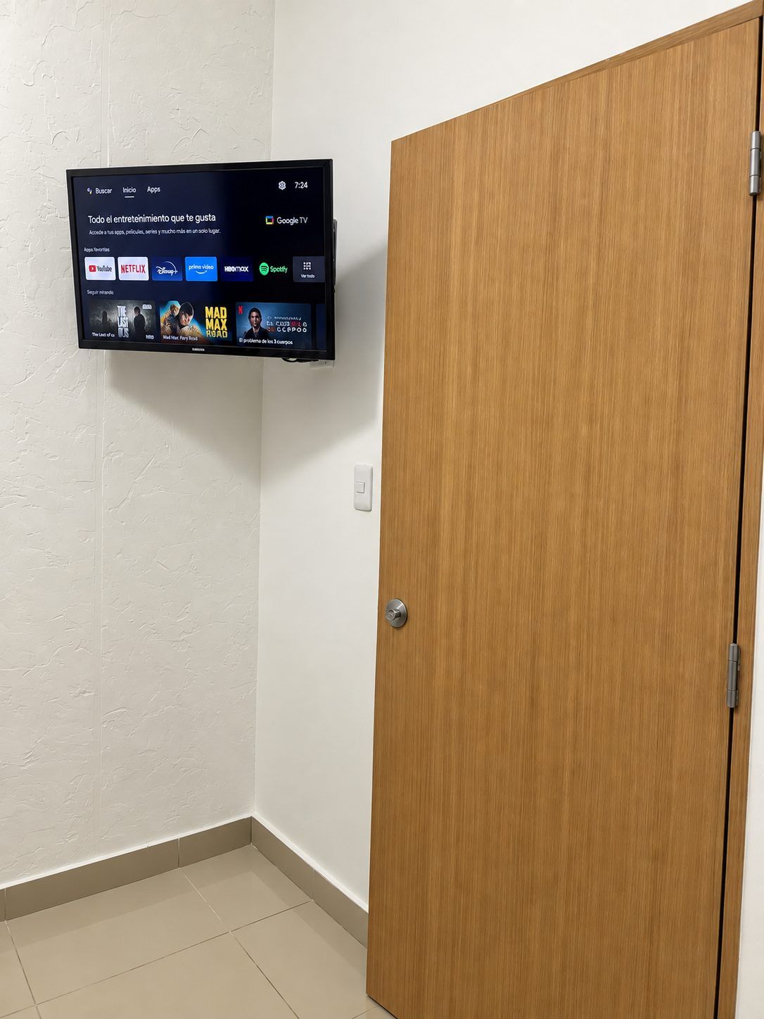 Een kamer met een televisie aan de muur waarop diverse streamingdiensten worden weergegeven en een houten deur.