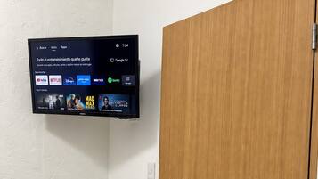 Een kamer met een televisie aan de muur waarop diverse streamingdiensten worden weergegeven en een houten deur.