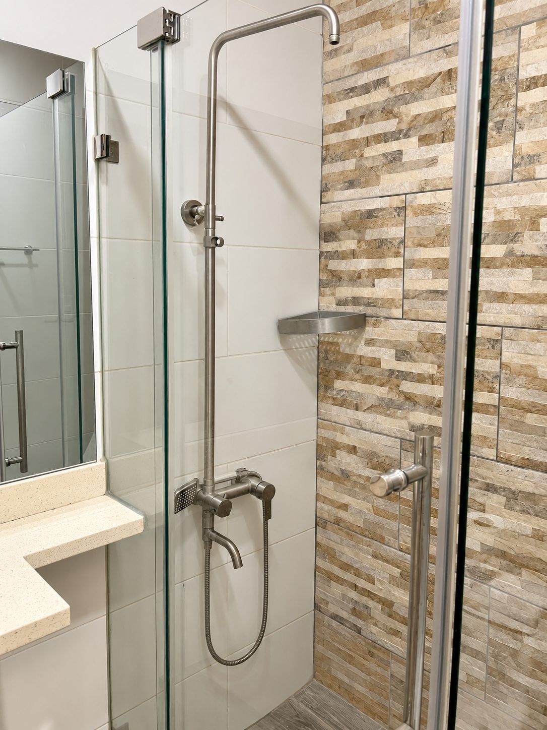 Een douche met een glazen deur, een handdouche en een bedieningspaneel op de muur.