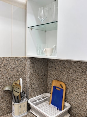 Een keuken met een wit kastje, een glazen plank en een accessoirehouder met een blauw snijplank.