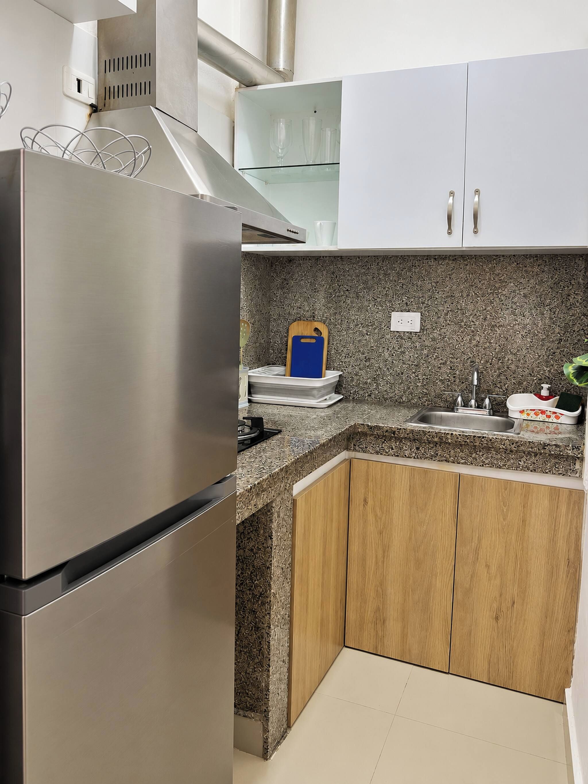 Una cocina con refrigerador de acero inoxidable, gabinetes de madera, encimera de granito y pileta empotrada.