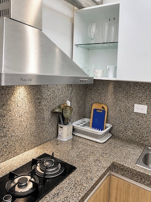 Een keuken met een roestvrijstalen afzuigkap, een granieten aanrecht en een afwasschuur met bestek.