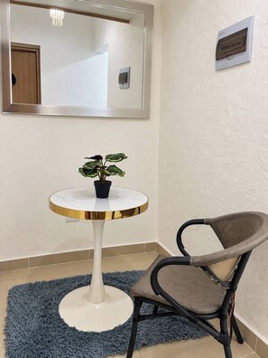 Quarto com uma mesa redonda, uma cadeira, planta em vaso, espelho e um dispositivo fixado na parede.