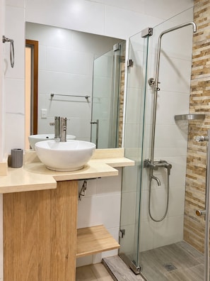 Een moderne badkamer met een glazen douchecabine, een witte wastafel en een houten opbergmeubel.