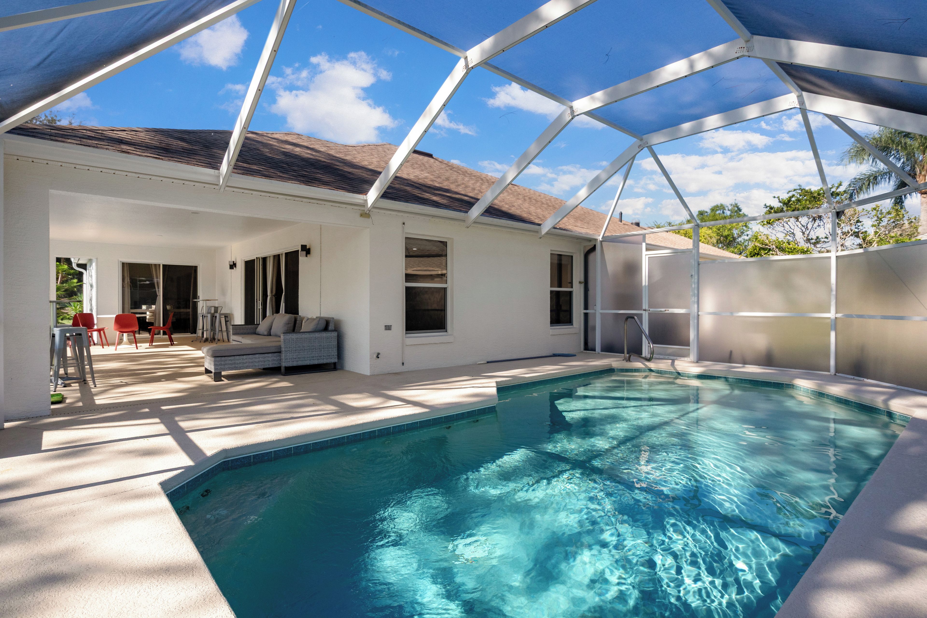 A covered outdoor swimming pool with a patio area, a covered seating area, and a view of the sky.