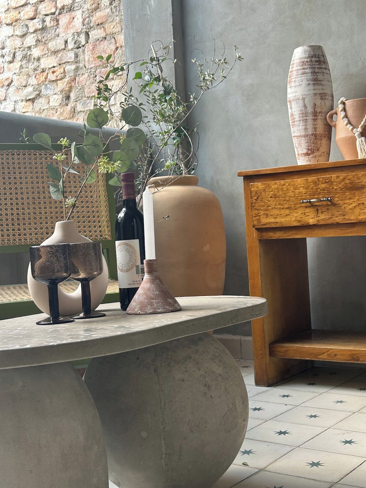 A room with a table, a potted plant, a wine bottle, and a vase.