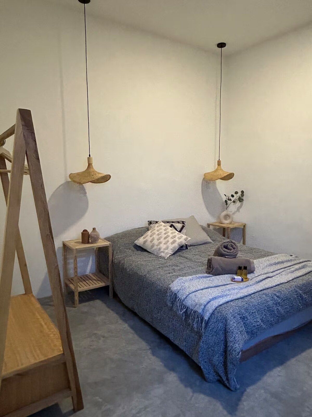 A bedroom with a bed, two bedside tables, a wooden ladder, and two hanging lamps.