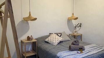A bedroom with a bed, two bedside tables, a wooden ladder, and two hanging lamps.
