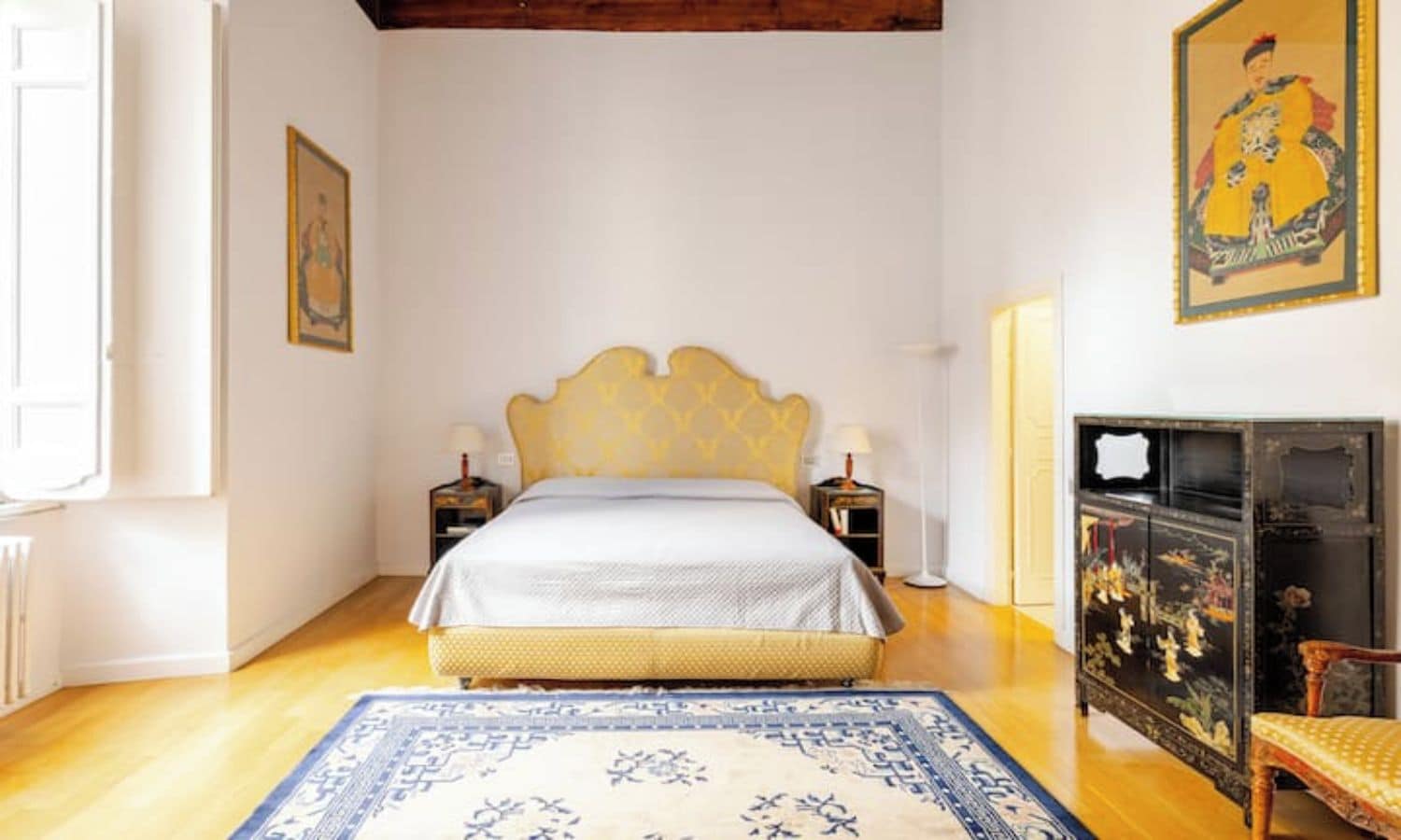 A bedroom with a bed, bedside tables, a rug, a chair, and a cabinet.