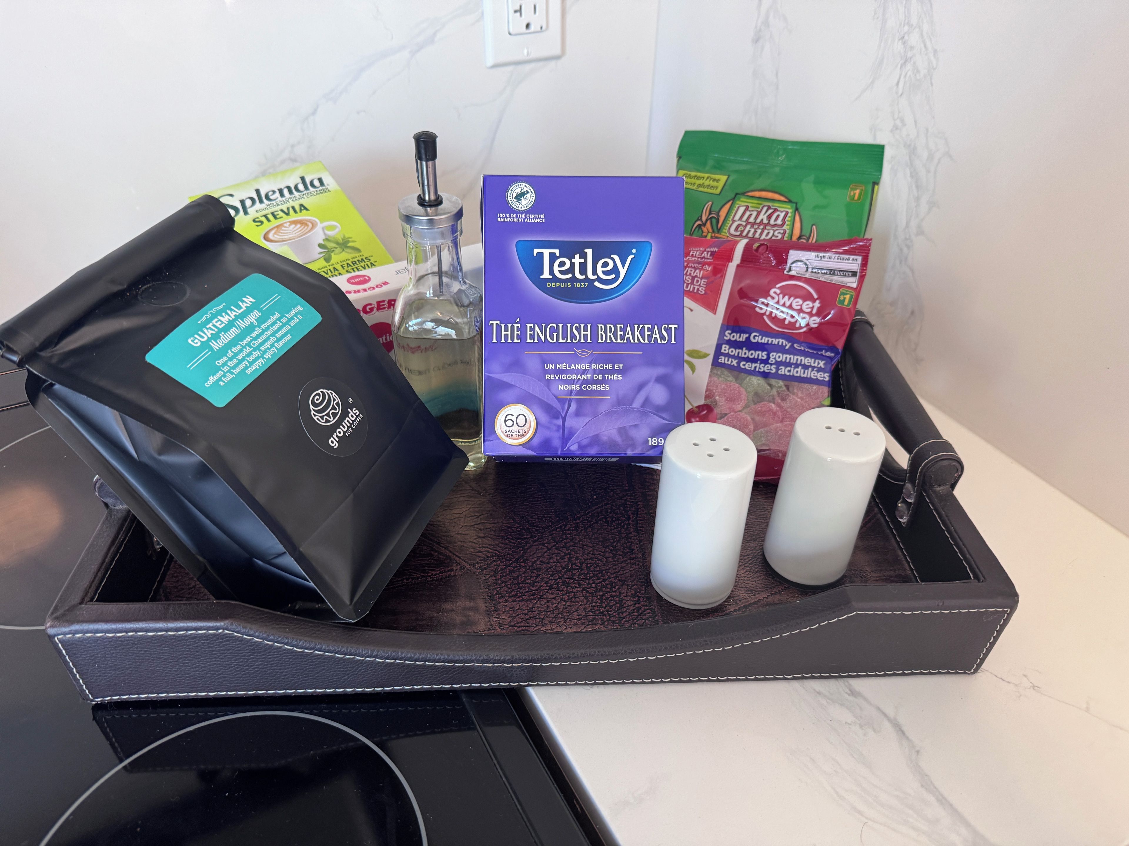 A tray with a coffee pod, a box of Tetley tea, a bag of Splenda, a bottle of water, and two salt shakers.