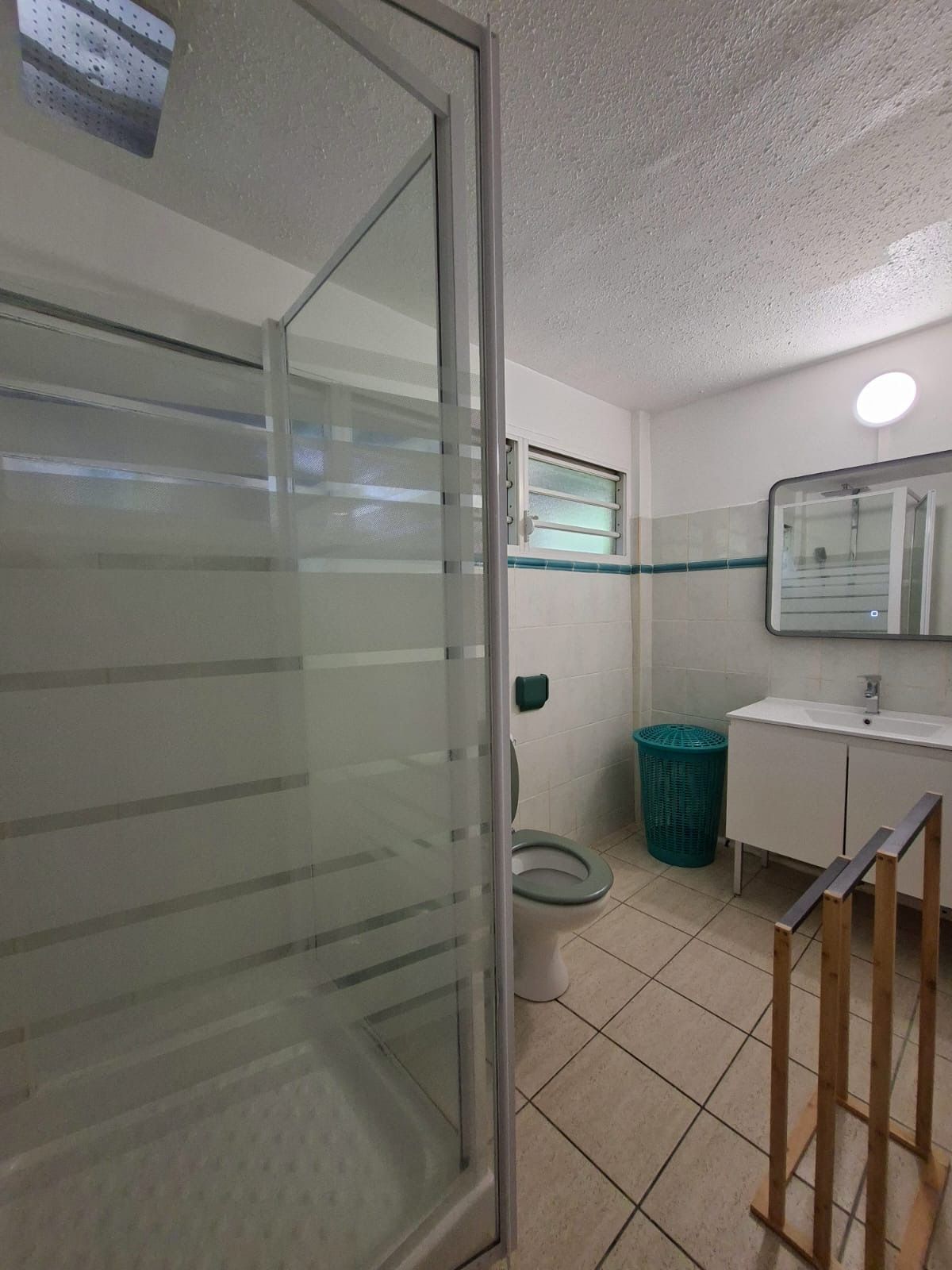 Un baño con cabina de ducha de vidrio, inodoro, lavabo con espejo y un cubo de basura.